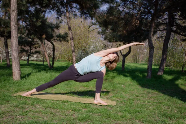 Joven mujer en forma hermosa haciendo yoga asans en el parque de pinos con estera de yoga — Foto de Stock