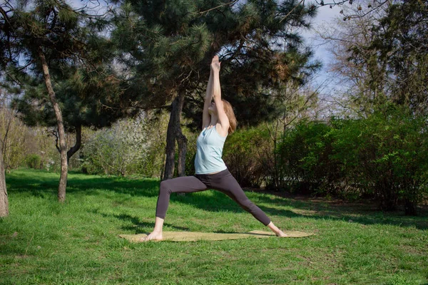 Joven mujer en forma hermosa haciendo yoga asans en el parque de pinos con estera de yoga —  Fotos de Stock