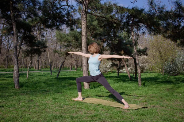 Joven mujer en forma hermosa haciendo yoga asans en el parque de pinos con estera de yoga — Foto de Stock