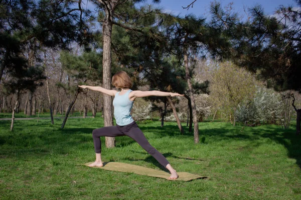 Joven mujer en forma hermosa haciendo yoga asans en el parque de pinos con estera de yoga — Foto de Stock