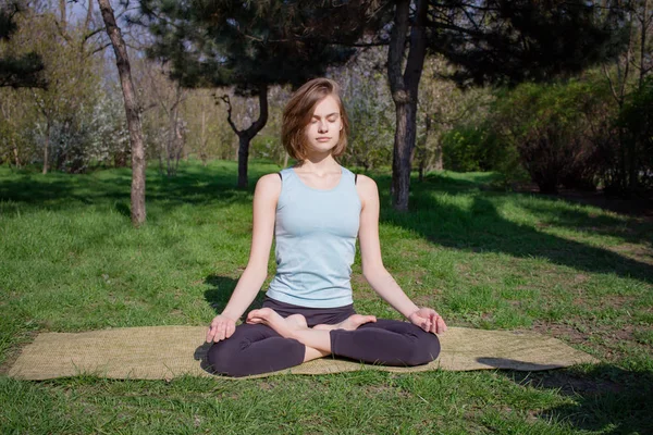 Молодая красивая женщина делает yoga asans в сосновом парке с циновкой yoga — стоковое фото