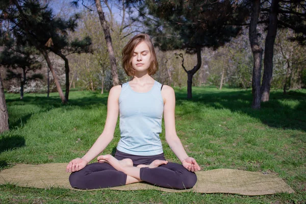 Giovane bella donna in forma facendo asans yoga nel parco dei pini con tappetino yoga — Foto Stock