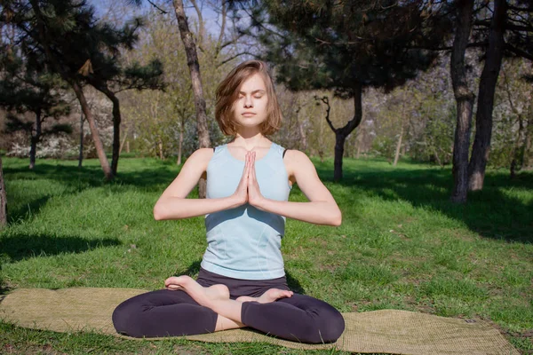 Giovane bella donna in forma facendo asans yoga nel parco dei pini con tappetino yoga — Foto Stock