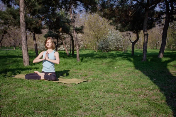 Junge schöne, fitte Frau macht Yoga-Asans im Kiefernpark mit Yogamatte — Stockfoto