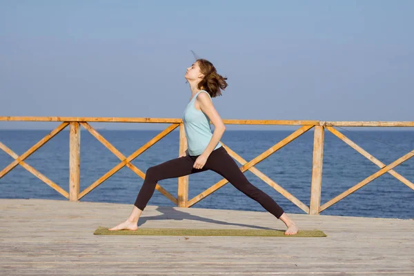 Genç seksi kadının deniz arka plan ve mavi gökyüzü karşı ahşap iskele üzerinde yoga egzersizleri yapması — Stok fotoğraf