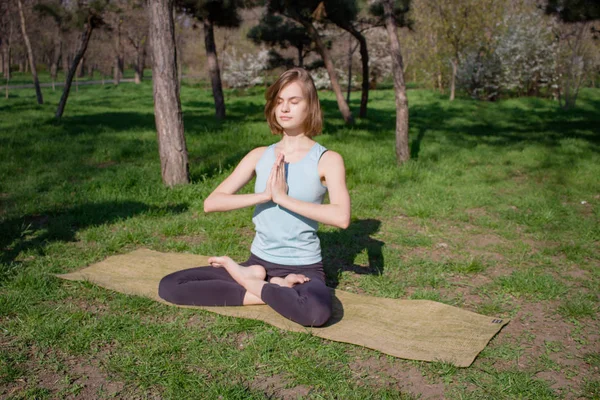 Giovane bella donna in forma facendo asans yoga nel parco dei pini con tappetino yoga — Foto Stock