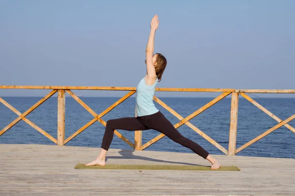 Tânăra femeie sexy face exerciții de yoga pe cheiul de lemn pe fundalul mării și cerul albastru — Fotografie, imagine de stoc