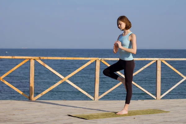 Genç seksi kadının deniz arka plan ve mavi gökyüzü karşı ahşap iskele üzerinde yoga egzersizleri yapması — Stok fotoğraf