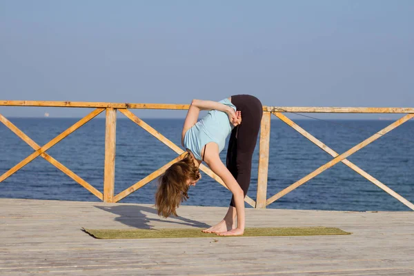 Young sexy woman doing yoga exercises on the wooden pier against sea background and blue sky — Stock Photo, Image