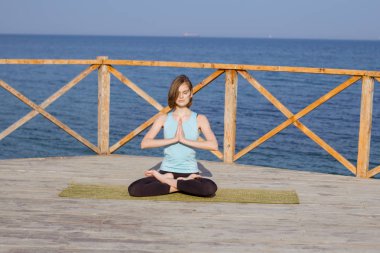 Genç seksi kadının deniz arka plan ve mavi gökyüzü karşı ahşap iskele üzerinde yoga egzersizleri yapması
