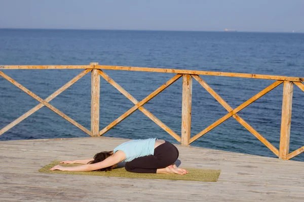 Νέοι σέξι γυναίκα κάνει Γιόγκα ασκήσεις στην ξύλινη προβλήτα κατά θάλασσα φόντο και μπλε ουρανό — Φωτογραφία Αρχείου