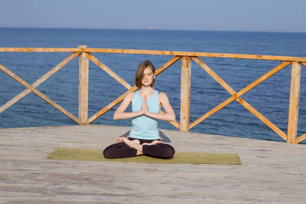 Genç seksi kadının deniz arka plan ve mavi gökyüzü karşı ahşap iskele üzerinde yoga egzersizleri yapması — Stok fotoğraf