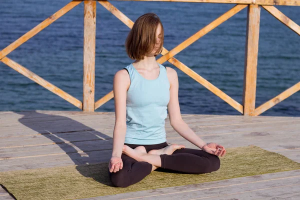 Tânăra femeie sexy face exerciții de yoga pe cheiul de lemn pe fundalul mării și cerul albastru — Fotografie, imagine de stoc