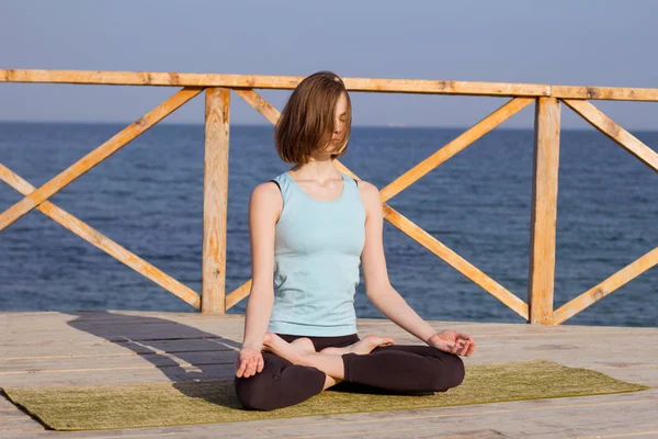 Mujer sexy joven haciendo ejercicios de yoga en el muelle de madera contra el fondo del mar y el cielo azul — Foto de Stock