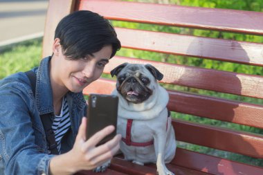 Pug genç kadın üzerinde cep telefonu, kadın ve köpek portre parkta selfie olun