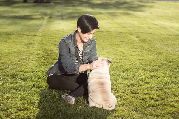 Junge Frau mit Mops im grünen Gras, hübsches Mädchen mit Hund beim Spielen im Park bei Sonnenuntergang oder Sonnenaufgang — Stockfoto