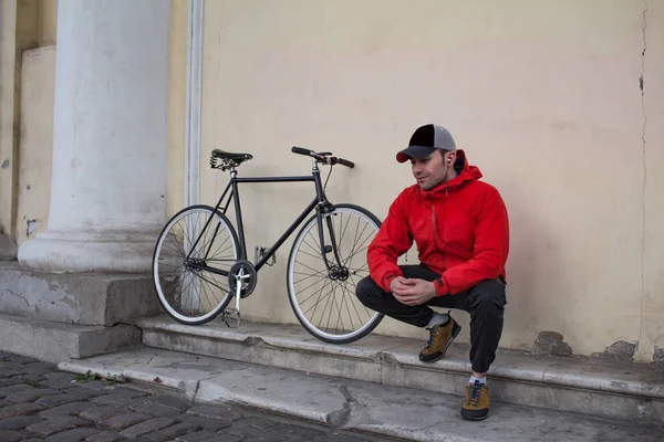 Mladý muž seděl na schodech budovy, černé bokové kolo na pozadí — Stock fotografie