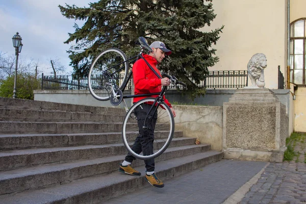 Jovem hipster descendo escadas com preto fixedgear bicicleta, velho europeu cidade fundo — Fotografia de Stock