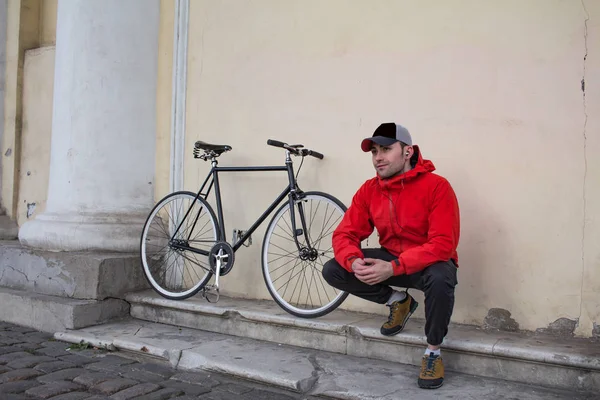 Mladý muž seděl na schodech budovy, černé bokové kolo na pozadí — Stock fotografie