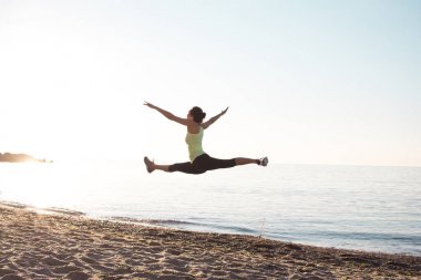 Genç profesyonel jimnastikçi kadın dans beach, eğitim çalışmaları ile serin junps, deniz ya da okyanus arka planda gündoğumu 