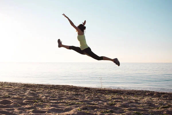 Joven gimnasta profesional mujer danza en la playa, ejercicios de entrenamiento con saltos fríos, salida del sol en el mar o el fondo del océano — Foto de Stock