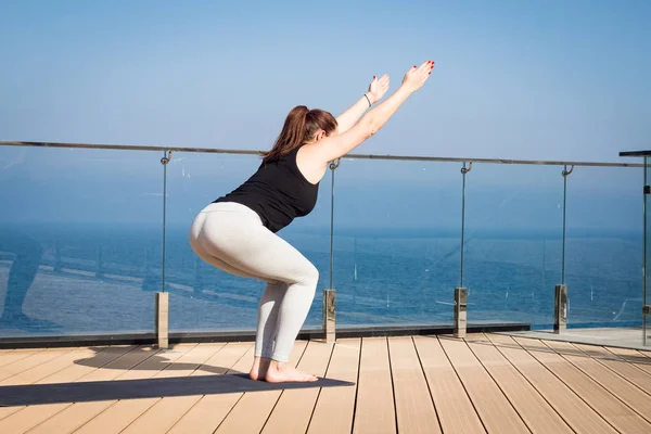 Mujer del deporte haciendo ejercicio de yoga estiramiento en el techo del hotel con soporte de piso de madera en la estera de yoga —  Fotos de Stock