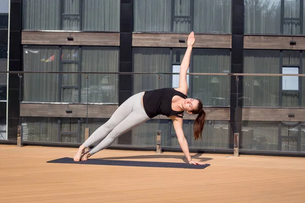 Mujer del deporte haciendo ejercicio de yoga estiramiento en el techo del hotel con soporte de piso de madera en la estera de yoga —  Fotos de Stock