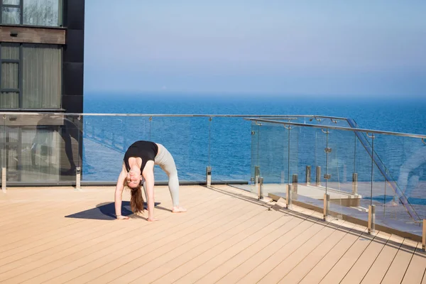 Mujer del deporte haciendo ejercicio de yoga estiramiento en el techo del hotel con soporte de piso de madera en la estera de yoga — Foto de Stock
