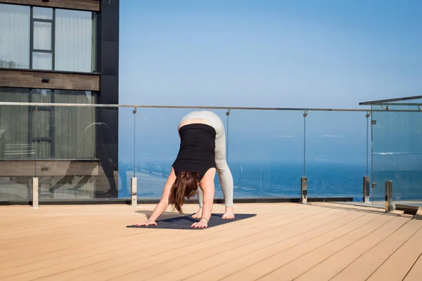 Mujer del deporte haciendo ejercicio de yoga estiramiento en el techo del hotel con soporte de piso de madera en la estera de yoga —  Fotos de Stock