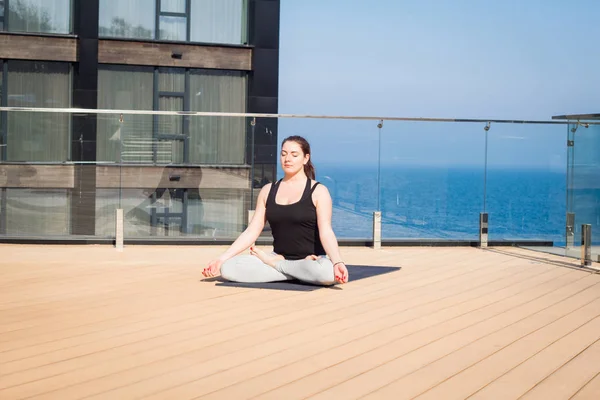 Mujer del deporte haciendo ejercicio de yoga estiramiento en el techo del hotel con soporte de piso de madera en la estera de yoga —  Fotos de Stock