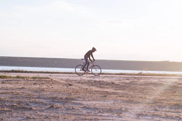 Alone rider on fixed gear road bike riding in the desert near river, hipster tourist bicycle rider pictures. — Stock Photo, Image