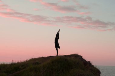Kadın egzersiz güzel dağlar peyzaj açık germe yoga yaparken uygun. Deniz ve gündoğumu veya günbatımı arka plan eğitim asans taşla kadın. Yoga pozlar kadın silüeti