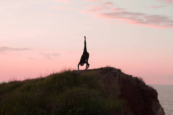 Mujer en forma haciendo ejercicio de estiramiento de yoga al aire libre en hermosos paisajes de montañas. Mujer en la roca con mar y amanecer o atardecer entrenamiento de fondo asans. Silueta de mujer en poses de yoga — Foto de Stock