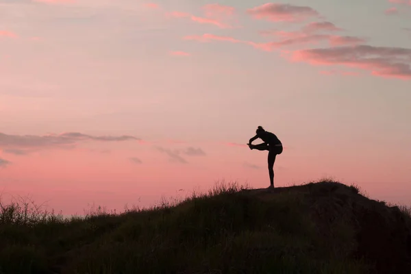 Passar kvinna som gör yoga stretching Motion utomhus i vackra landskap. Kvinna på vagga med havet och soluppgång eller solnedgång bakgrund utbildning asans. Siluett av kvinna i yogaställningarna — Stockfoto