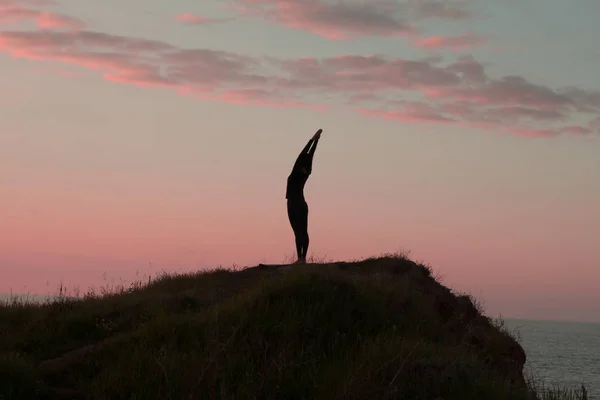 Mujer en forma haciendo ejercicio de estiramiento de yoga al aire libre en hermosos paisajes de montañas. Mujer en la roca con mar y amanecer o atardecer entrenamiento de fondo asans. Silueta de mujer en poses de yoga — Foto de Stock