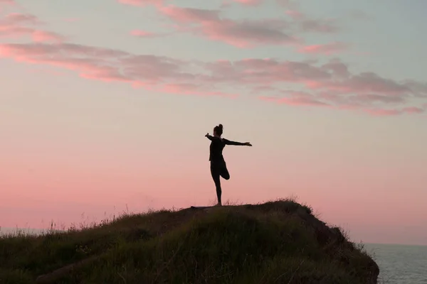 Fit femeie care face yoga stretching exerciții în aer liber în peisaj frumos munți. Femeie pe stâncă cu mare și răsărit sau apus de soare de fundal de formare asans. Silueta femeii în pozele yoga — Fotografie, imagine de stoc