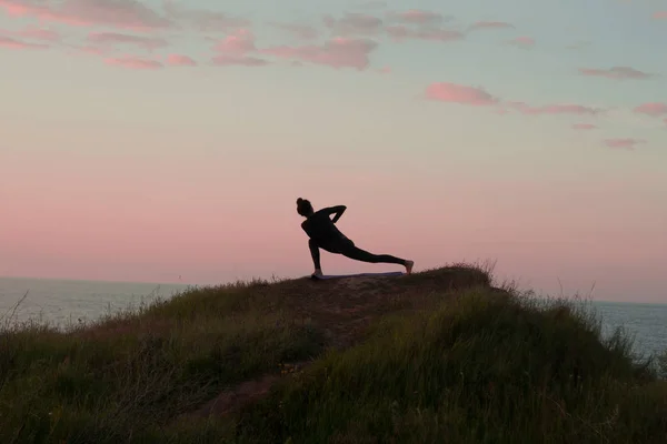 Fit femeie care face yoga stretching exerciții în aer liber în peisaj frumos munți. Femeie pe stâncă cu mare și răsărit sau apus de soare de fundal de formare asans. Silueta femeii în pozele yoga — Fotografie, imagine de stoc
