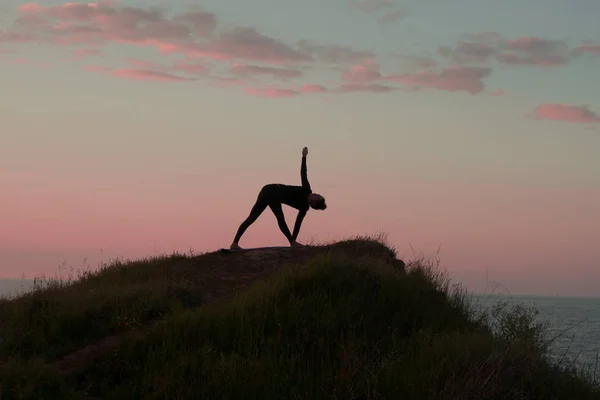 Подходящая женщина, занимающаяся йогой растягивая упражнения на открытом воздухе в красивом горном ландшафте. Женщина на скале с морем и восходом солнца или закатом фон обучения asans. Силуэт женщины в позах йоги — стоковое фото