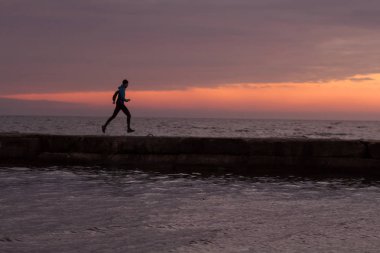 Sabah, gündoğumu karşı deniz ya da okyanus plajda genç erkek atlet. 