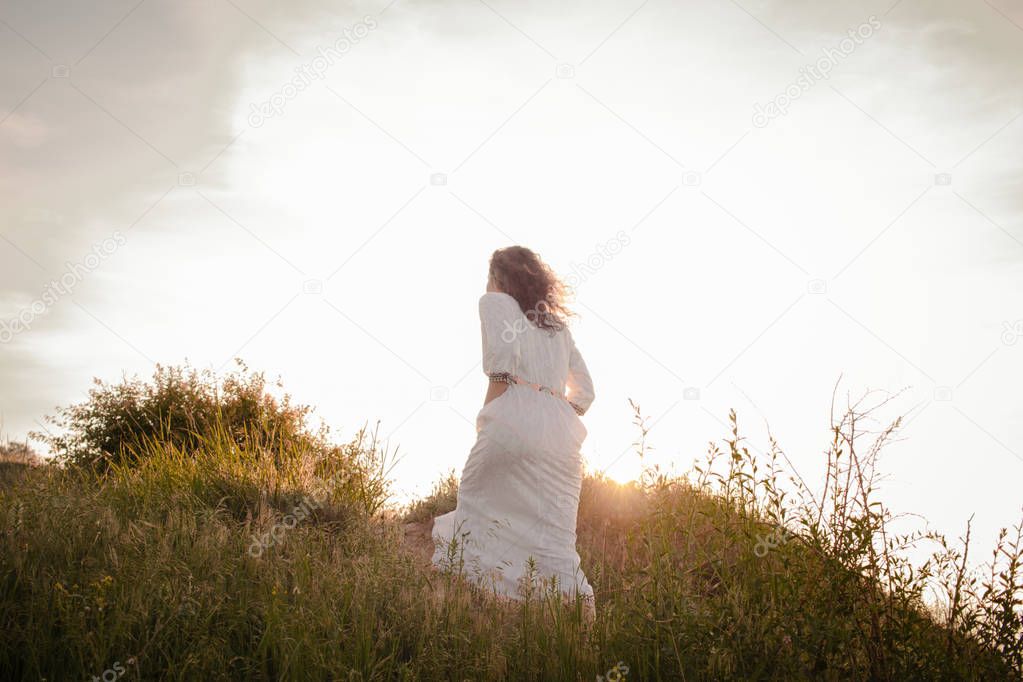 young woman walking on the morning beach in beautiful white dress. Fit female having good time during turing the sunrise.