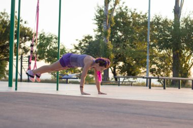 egzersiz süspansiyon ile açık spor salonunda formda kadın sabah erkenden parkta gündoğumu arka plan üzerinde eğitim kayışlar