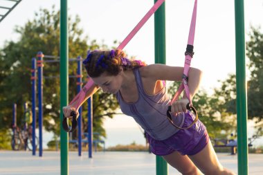 egzersiz süspansiyon ile açık spor salonunda formda kadın sabah erkenden parkta gündoğumu arka plan üzerinde eğitim kayışlar