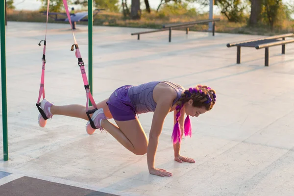 workout with suspension straps In the outdoor gym, fit woman training early in morning on the park, sunrise background