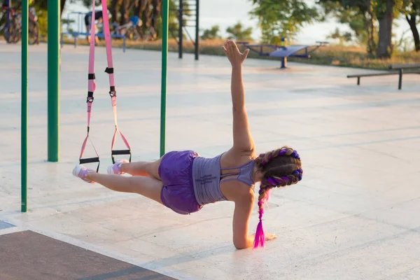 workout with suspension straps In the outdoor gym, fit woman training early in morning on the park, sunrise background