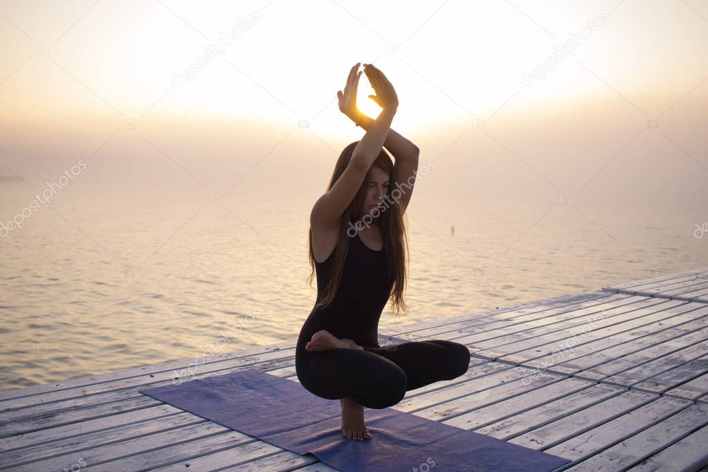 beautiful young woman in slim black wear doing yoga fitness during sunrise in fog.