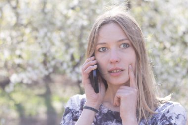 Genç kadın ile smartphone Bahar park, poz çiçekler arka plan üzerinde beyaz 