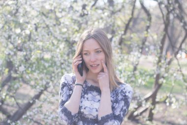 Genç kadın ile smartphone Bahar park, poz çiçekler arka plan üzerinde beyaz 