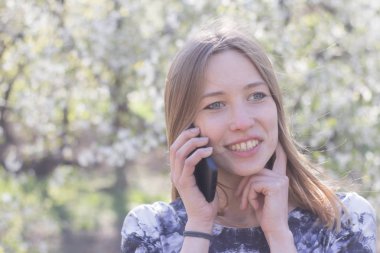 Genç kadın ile smartphone Bahar park, poz çiçekler arka plan üzerinde beyaz 