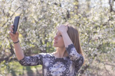 Genç kadın ile smartphone Bahar park, poz çiçekler arka plan üzerinde beyaz 