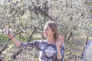 Genç kadın ile smartphone Bahar park, poz çiçekler arka plan üzerinde beyaz 